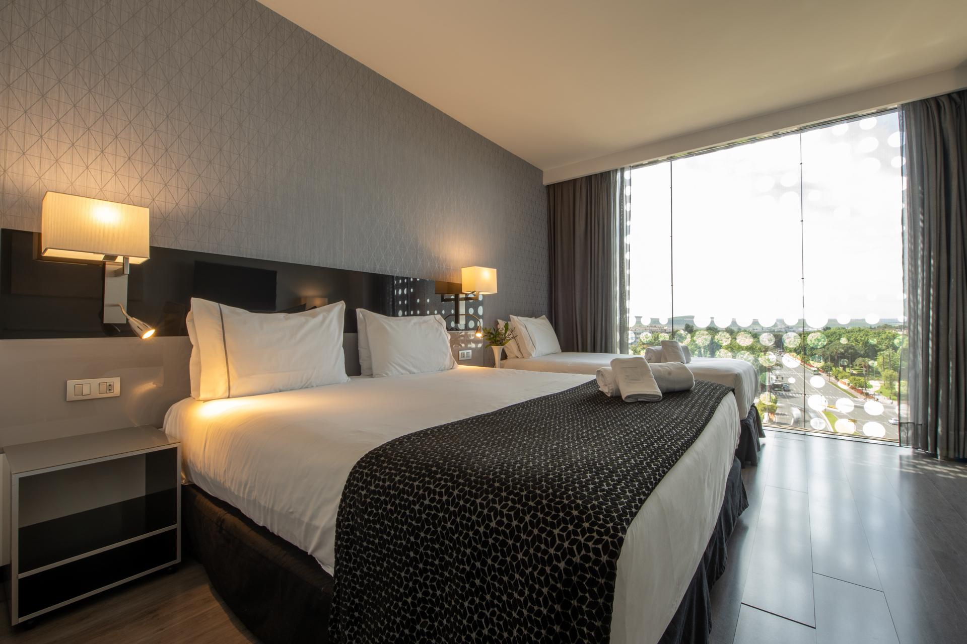 Eurostars Palace Кордоба Екстериор снимка The photo shows a modern hotel room featuring two large beds with white linens and dark patterned bedspreads. Each bed has a set of pillows and a decorative cushion. There are bedside lamps on either side of the beds, and a contemporary piece of furn