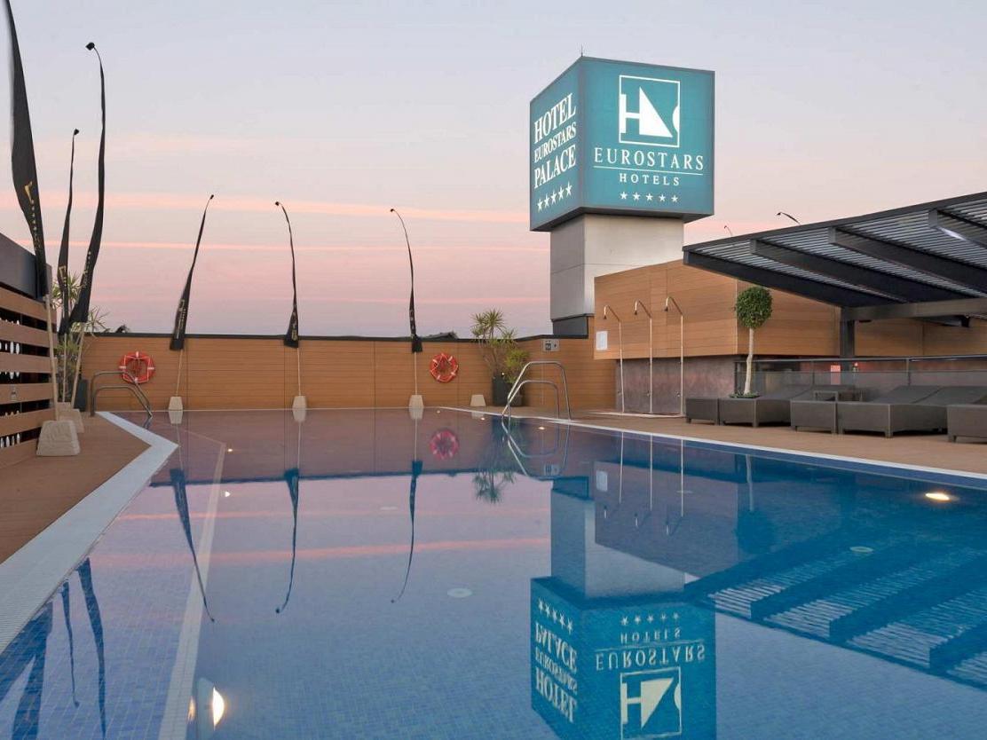 Eurostars Palace Кордоба Екстериор снимка The image shows a hotel pool area at twilight. The pool is large and reflective, capturing the colors of the sky and surrounding features. In the background, there is a hotel sign displaying the Eurostars brand, with a modern architecture style. The 