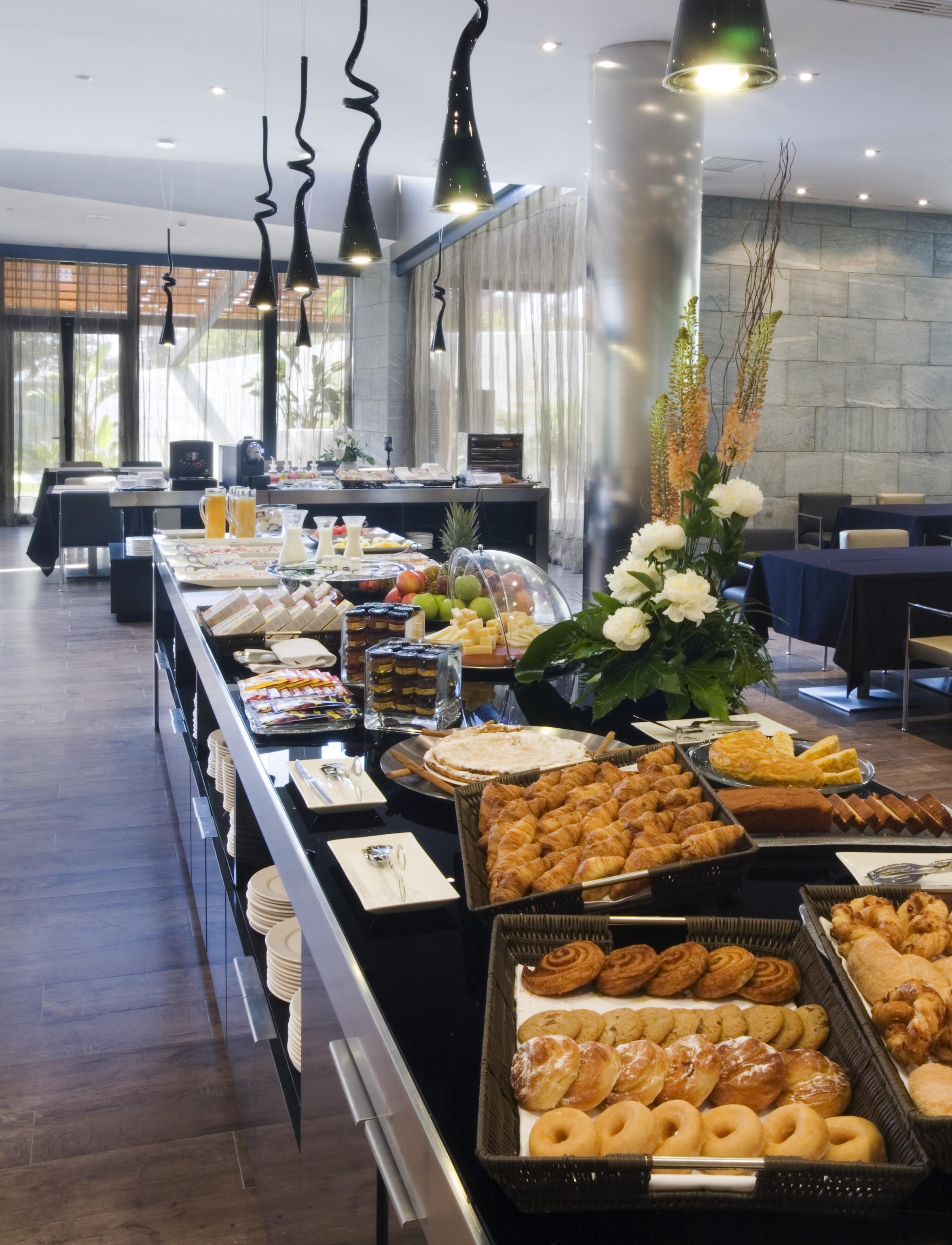 Eurostars Palace Кордоба Екстериор снимка The photo shows a beautifully arranged buffet spread in a modern setting. There are various dishes displayed on a long table, including pastries, desserts, fruits, and baked goods. A decorative arrangement of flowers enhances the presentation. The ba