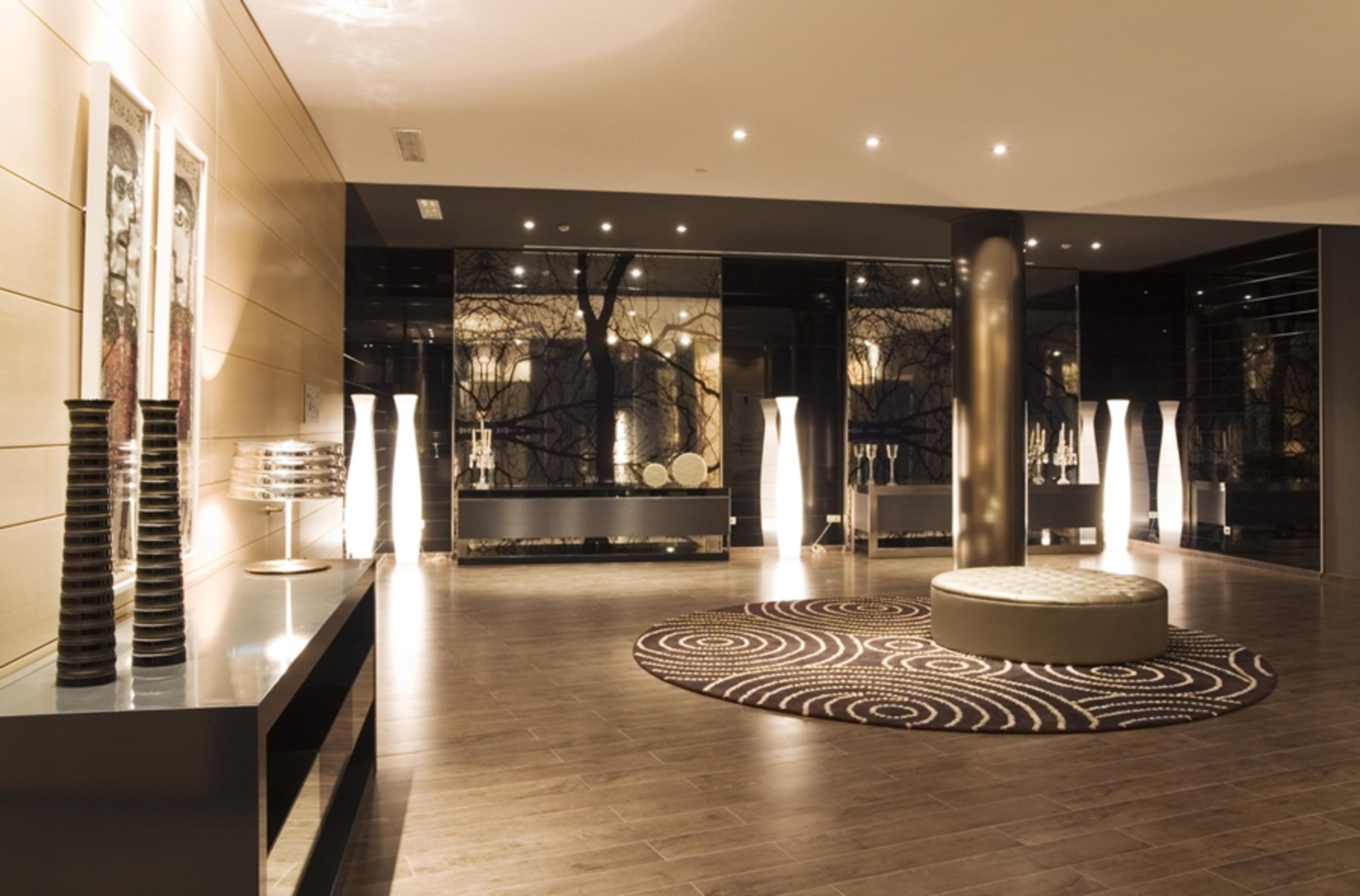 Eurostars Palace Кордоба Екстериор снимка The photo shows a modern interior space, likely a lobby or waiting area. The design features polished wooden flooring and sleek surfaces. There are tall, artistic light fixtures scattered throughout, contributing to a sophisticated ambiance. A round 