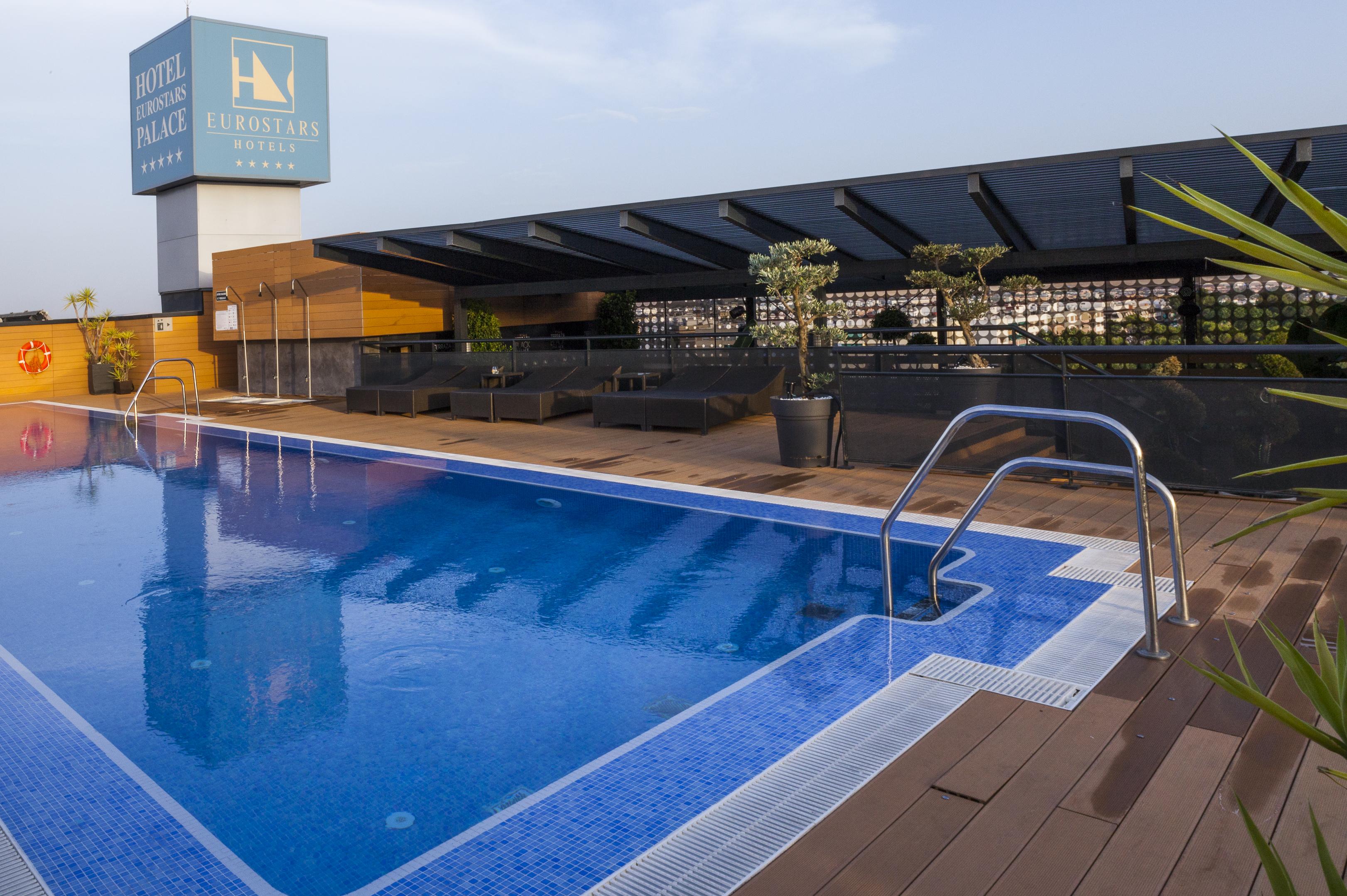Eurostars Palace Кордоба Екстериор снимка The photo shows a rooftop swimming pool with a clear blue water surface. There is a section of the pool with a ladder for entry, and the surrounding area includes wooden decking. In the background, there is a sign for a hotel, which appears to be nam