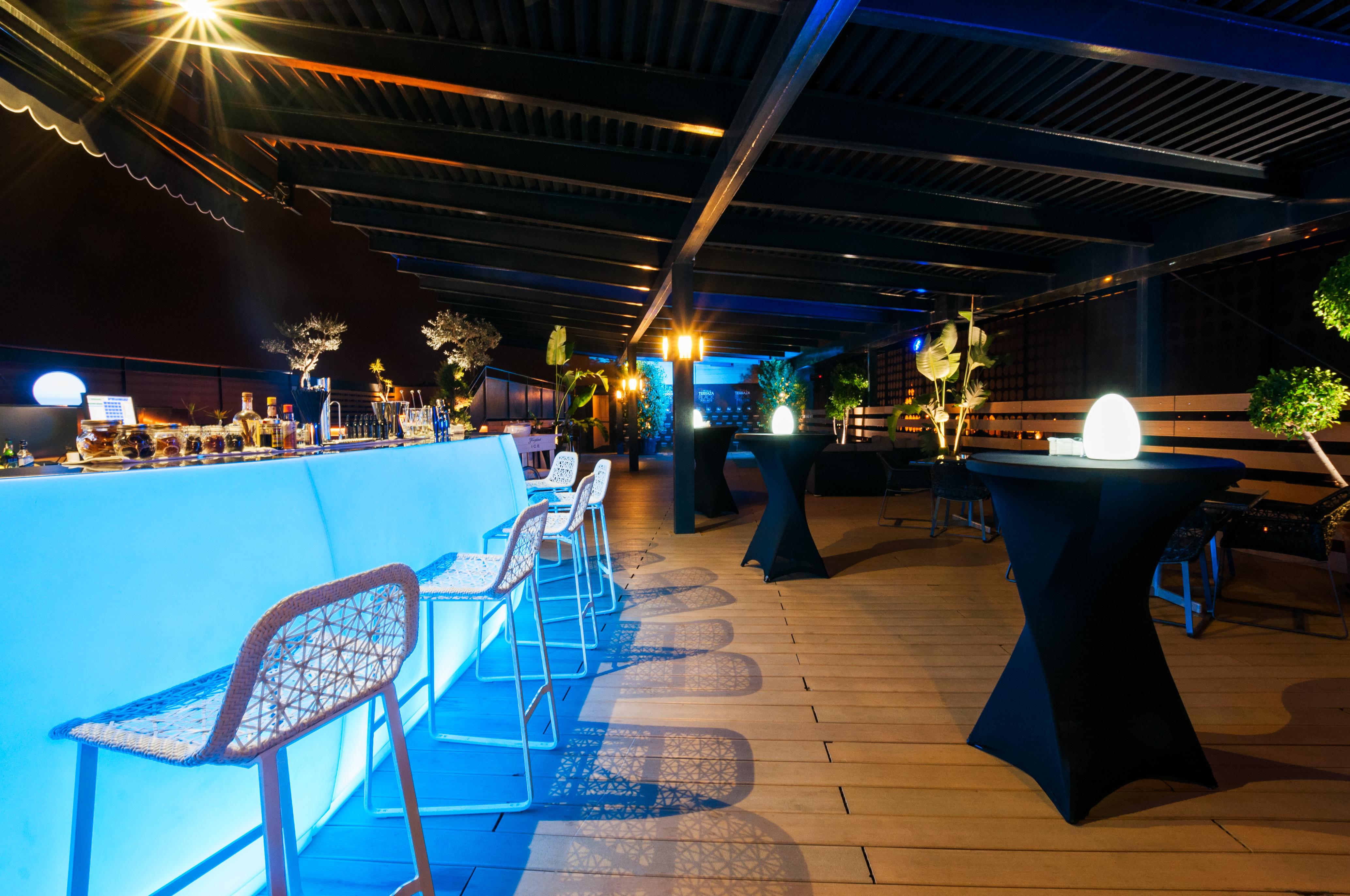 Eurostars Palace Кордоба Екстериор снимка The photo shows a stylish rooftop or outdoor bar area. There is a long bar counter illuminated with blue lighting, complemented by modern bar stools. The space is decorated with potted plants and elegant round tables covered in black cloth. Soft ligh
