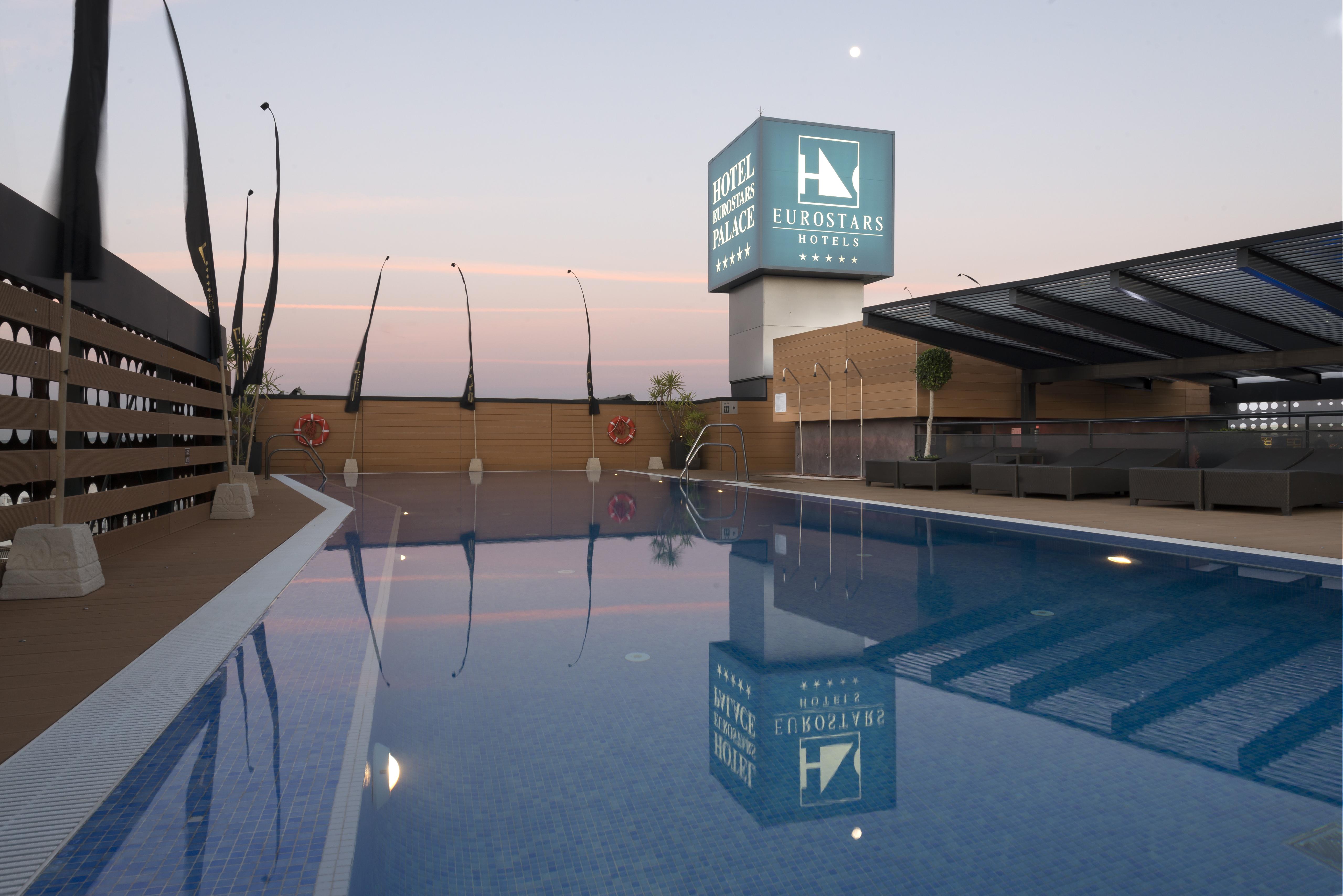Eurostars Palace Кордоба Екстериор снимка The photo shows a rooftop space featuring a swimming pool. The pool has a clear blue water, and the area around it is designed with modern aesthetics, including a wooden deck and comfortable seating. In the background, there is a prominent sign for "