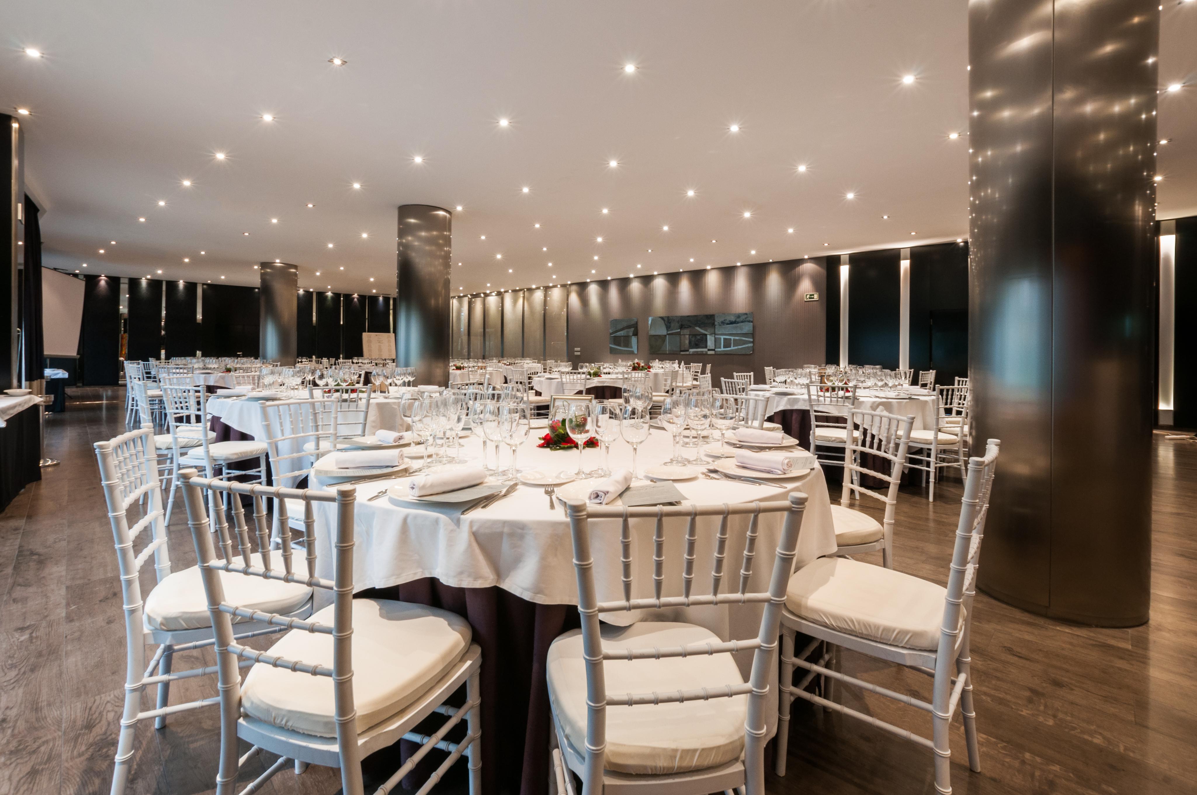 Eurostars Palace Кордоба Екстериор снимка The photo shows an elegant dining setting in a spacious restaurant. There are several round tables, each with white tablecloths and neatly arranged place settings, including glasses, plates, and utensils. The chairs are white with padded seats, provi