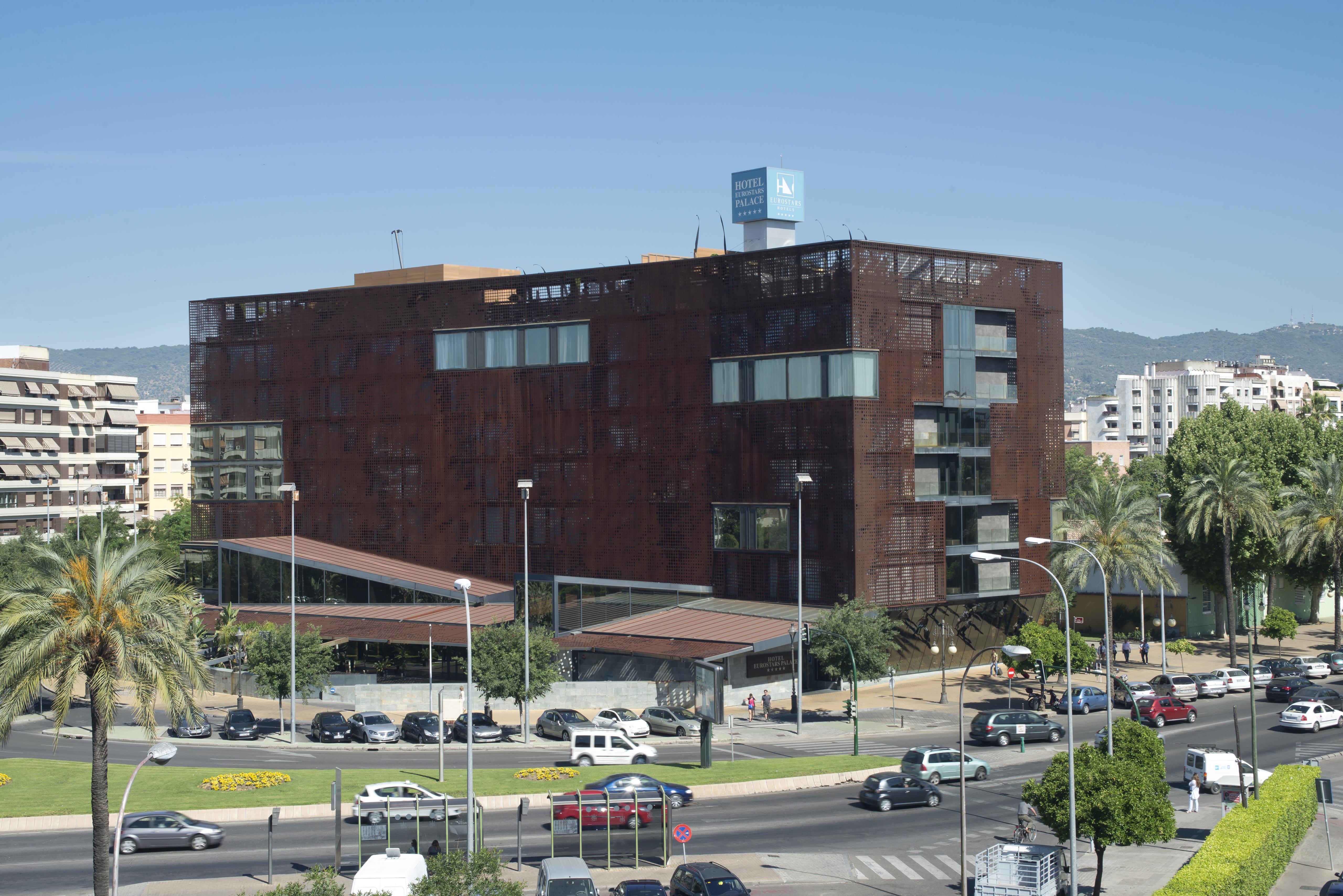Eurostars Palace Кордоба Екстериор снимка The photo shows a modern building characterized by a distinctive brown, rust-like exterior, which gives it an industrial appearance. The structure has multiple large windows, allowing for natural light to enter. There are several palm trees surroundi
