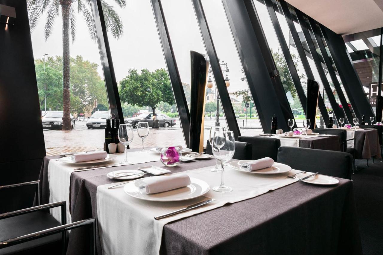 Eurostars Palace Кордоба Екстериор снимка The photo shows an elegant restaurant interior with large windows featuring modern angular designs. There are two dining tables set up, each covered with white and dark tablecloths. The tables are elegantly arranged with plates, cutlery, and wine gla
