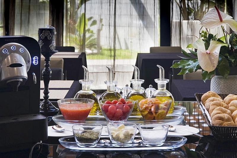 Eurostars Palace Кордоба Екстериор снимка The photo displays a stylish breakfast or brunch spread on a table. In the foreground, several small glass containers hold various ingredients: there are glasses filled with different types of oil, a bowl of fresh red tomatoes, a bowl of mixed fruit,