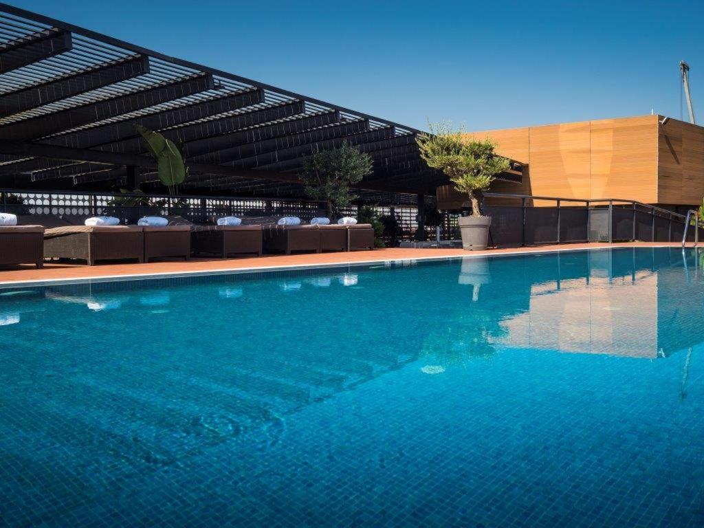Eurostars Palace Кордоба Екстериор снимка The photo shows a rooftop swimming pool with a clear, vibrant blue surface reflecting the sky. Surrounding the pool are comfortable lounge chairs, some shaded by a modern overhead structure. The area is accented with potted plants, adding greenery to