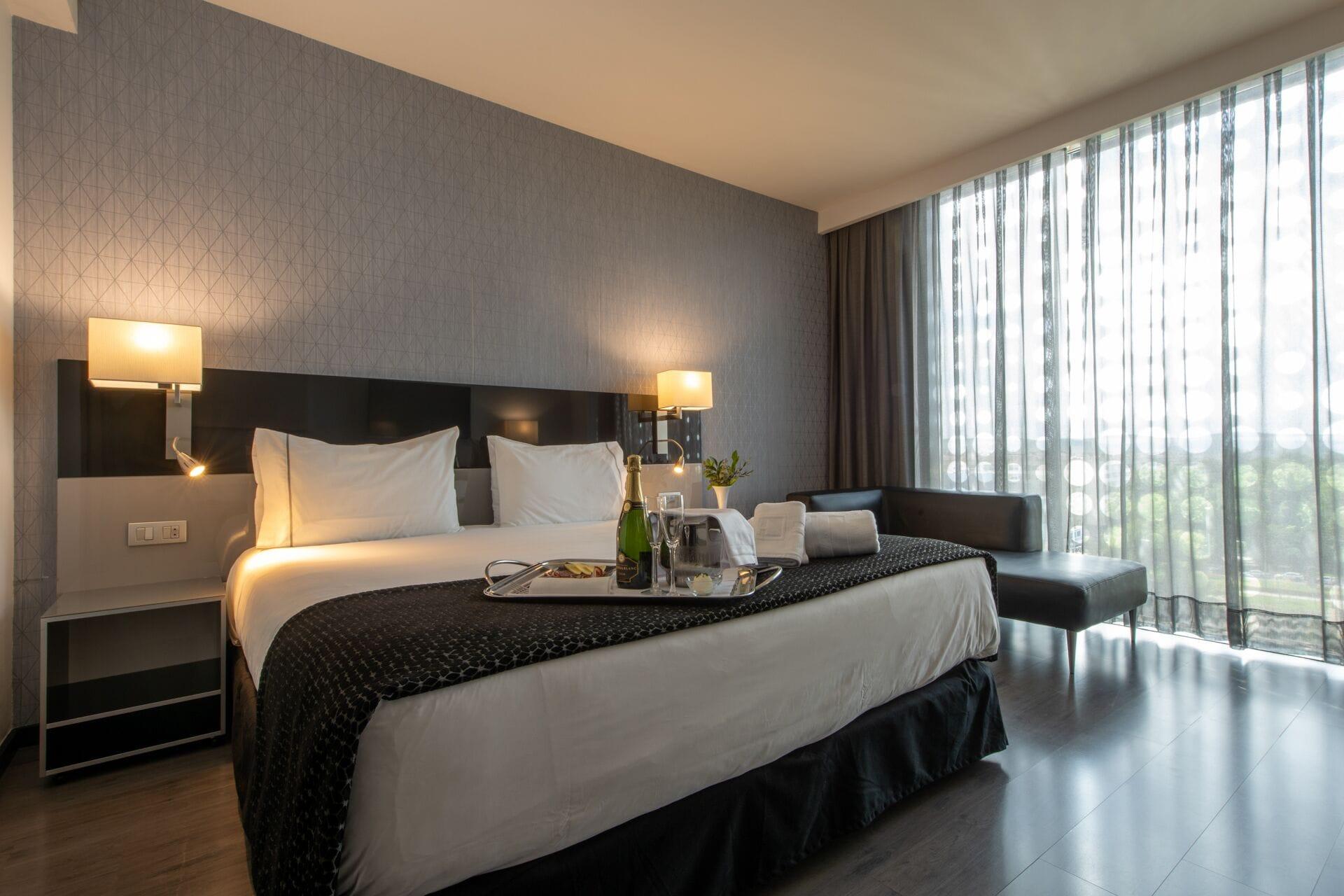 Eurostars Palace Кордоба Екстериор снимка The photo shows a modern hotel room featuring a large bed with crisp white linens and dark throw blankets. On either side of the bed, there are bedside lamps providing soft lighting. The room has a sleek design with a neutral color palette, including