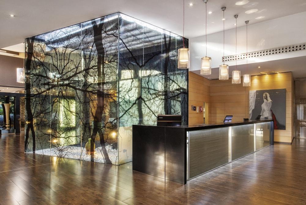 Eurostars Palace Кордоба Екстериор снимка The photo shows a stylish hotel lobby with a modern design. Central to the image is a prominent reception desk made of dark materials, featuring sleek lines and a well-lit front. Behind the desk is a striking glass wall featuring an artistic design r